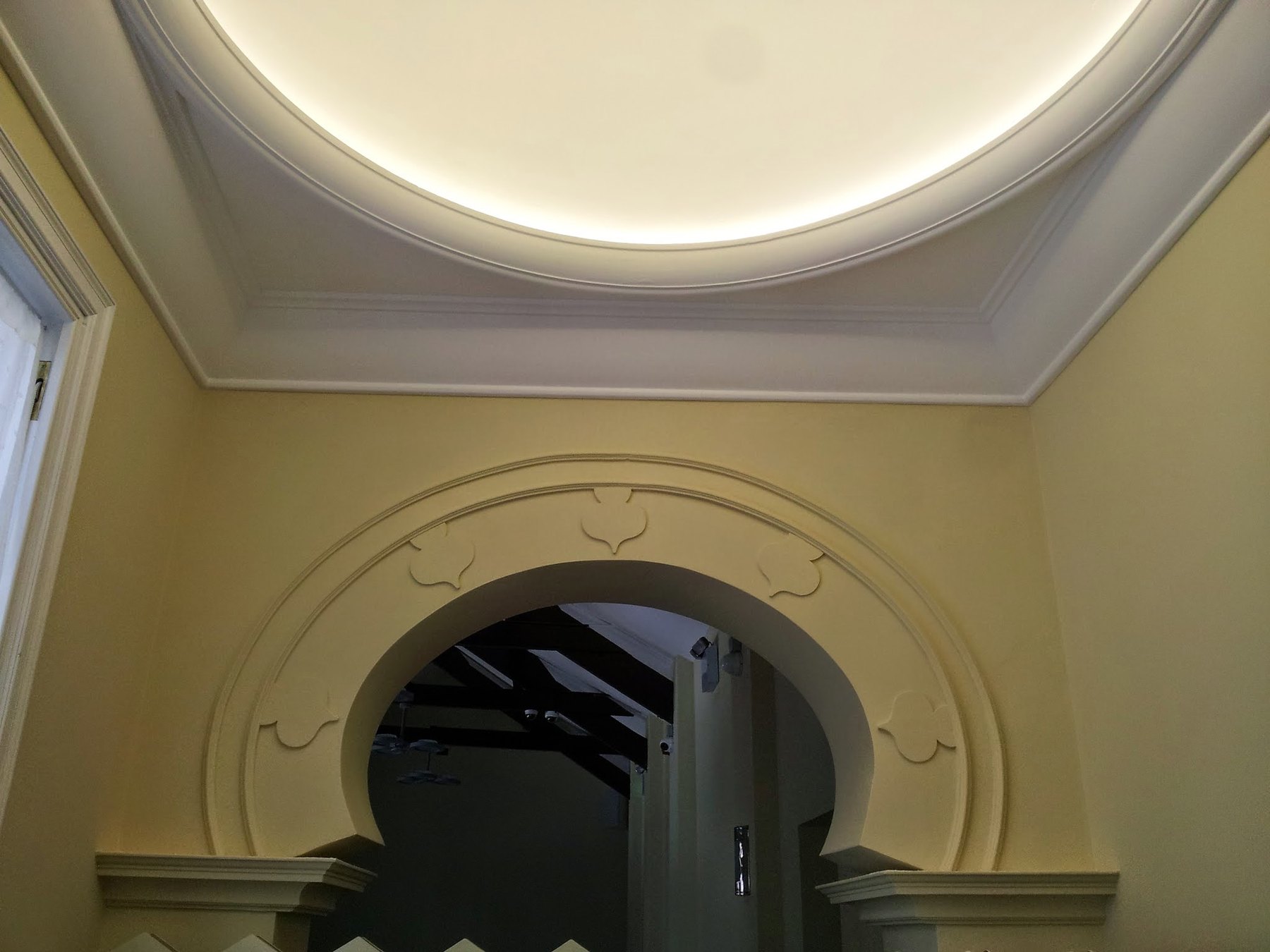 A moulded horseshoe arch in a room with a lit, domed ceiling and stepped cornice