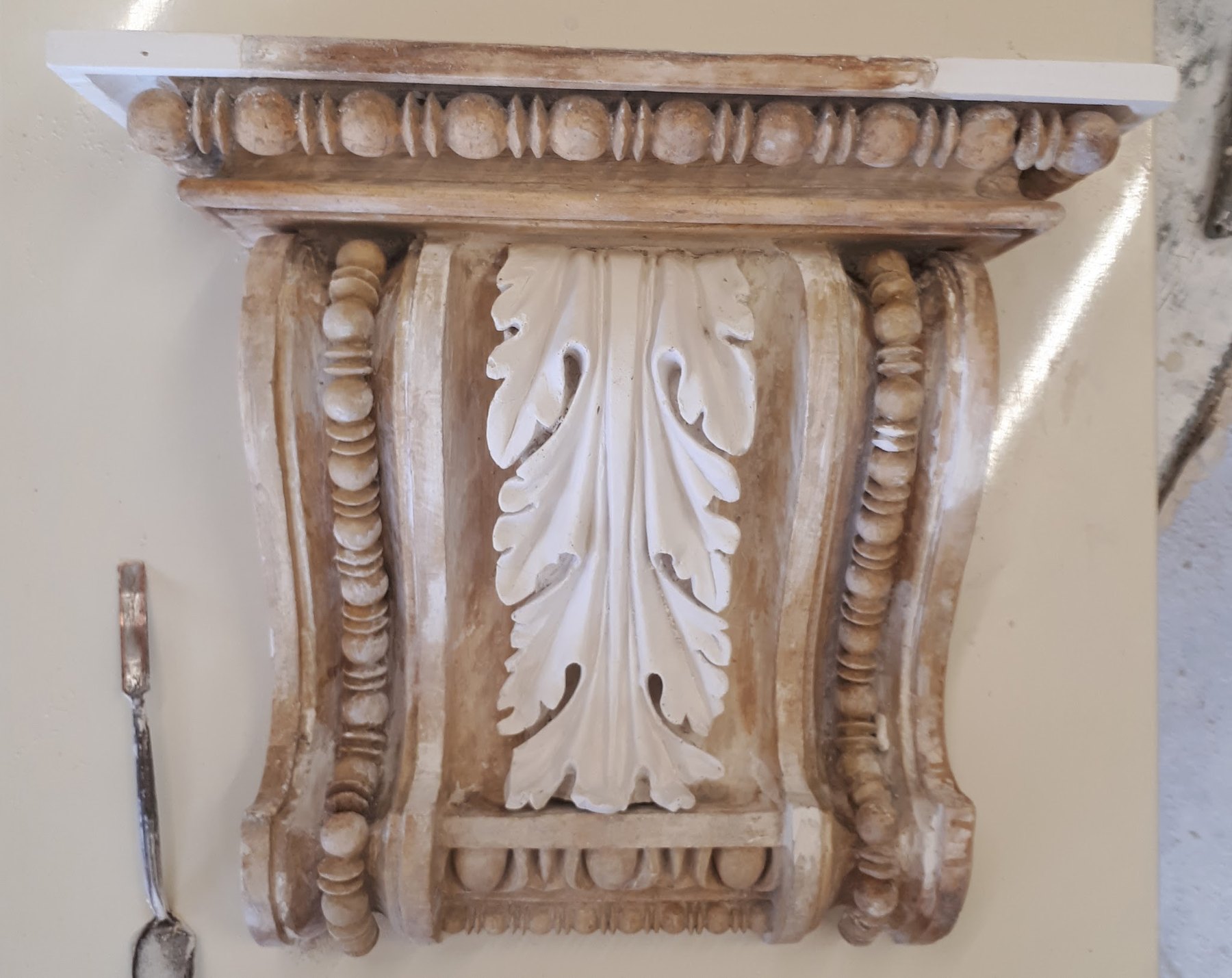 A large acanthus corbel fixed to a wall and picked out in cream and gold