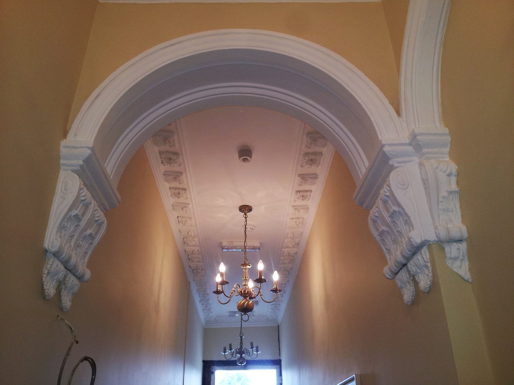 A hallway arch carried on two large acanthus corbels, with a decorated ceiling and chandelier beyond
